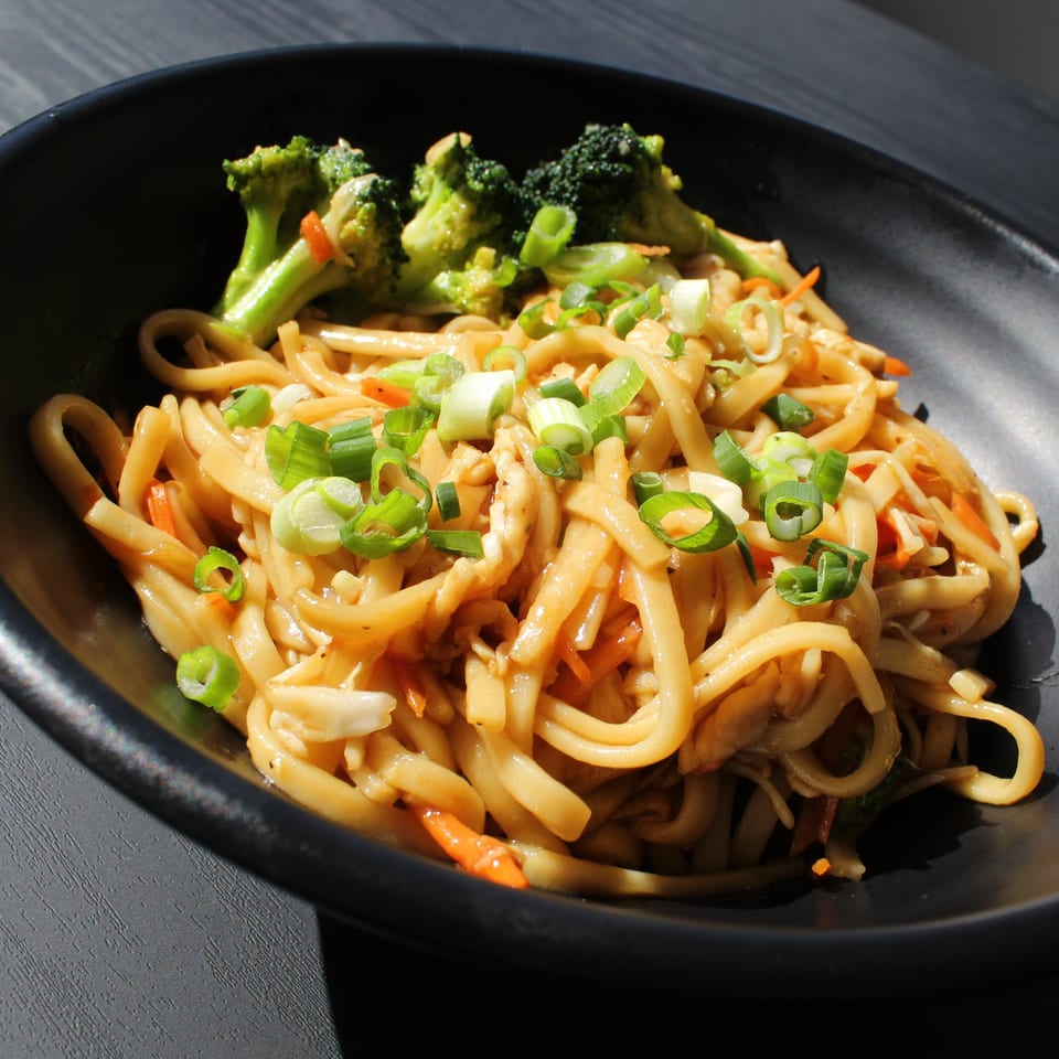 Roll N Wok's Asian-fusion noodles with broccoli, carrots, and green onions in a black bowl.