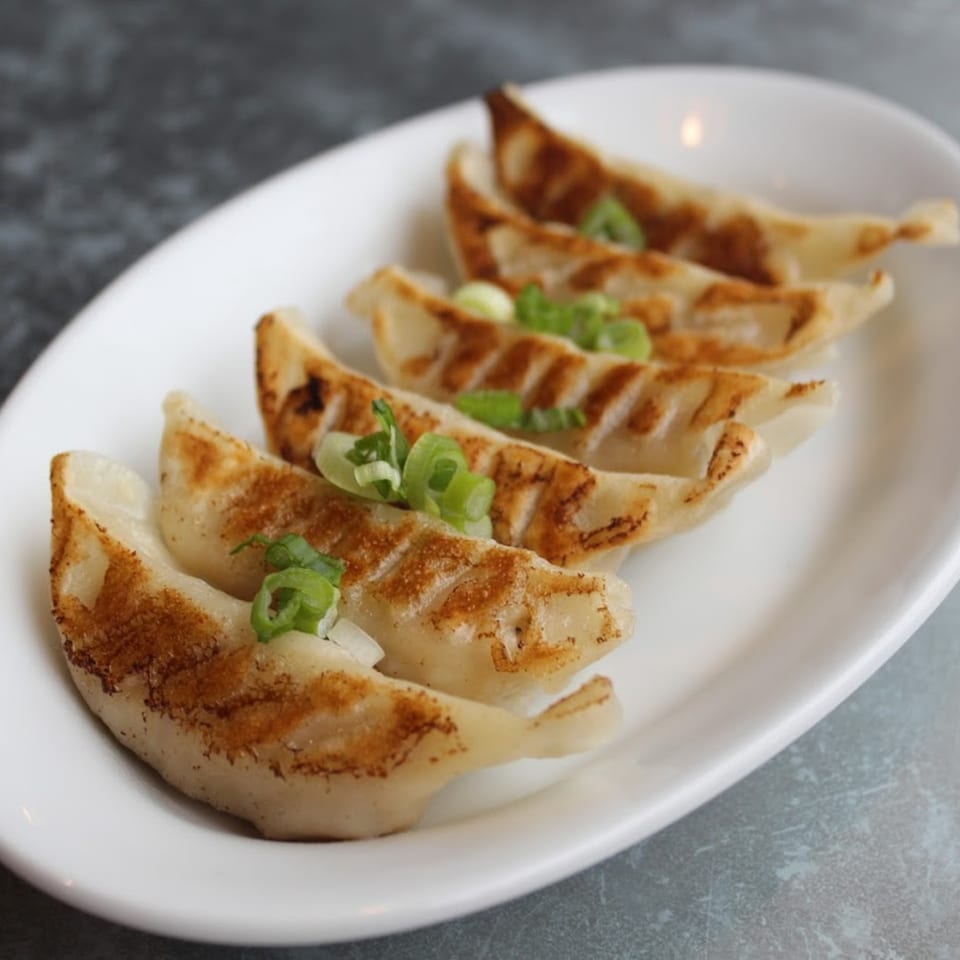 Pan-fried gyoza dumplings with crispy bottoms and green onion garnish on a white plate.